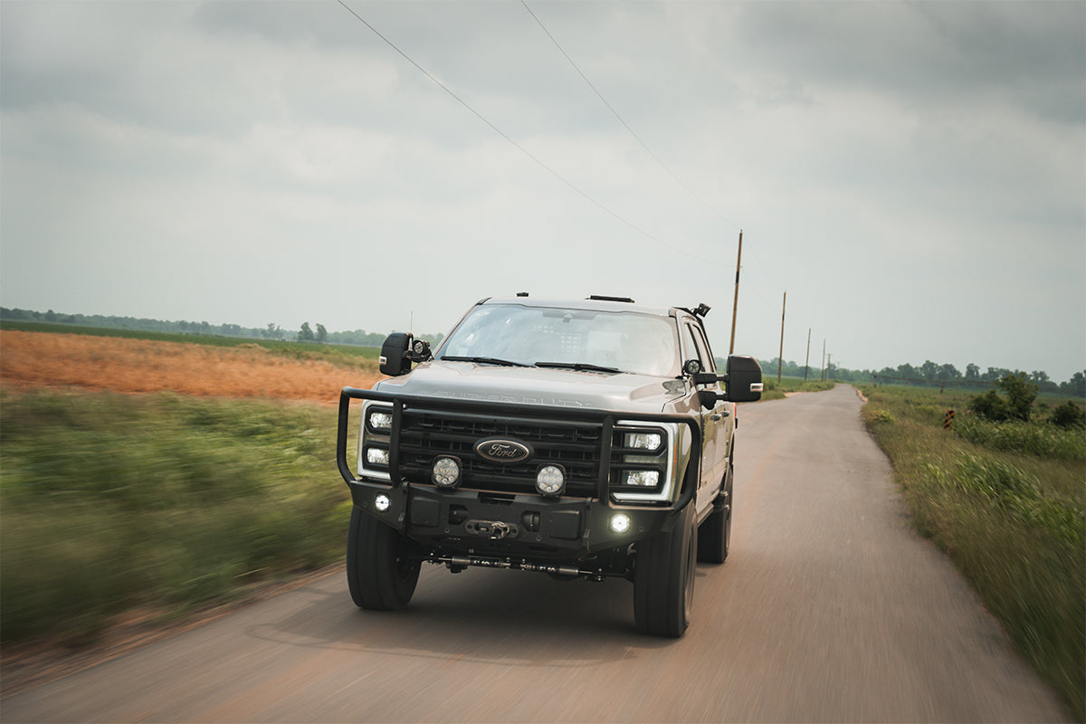 AGwagon Superduty drives down a highway next to farms and fields with storm grey clouds above.