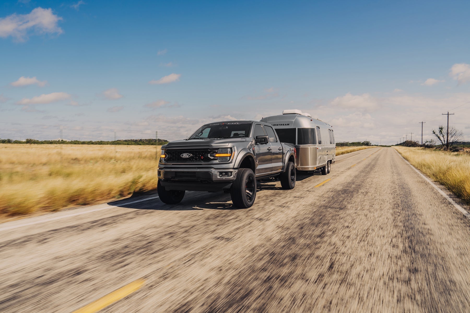 Grey Black Widow F-150 towing an Airstream camper rv down a highway.