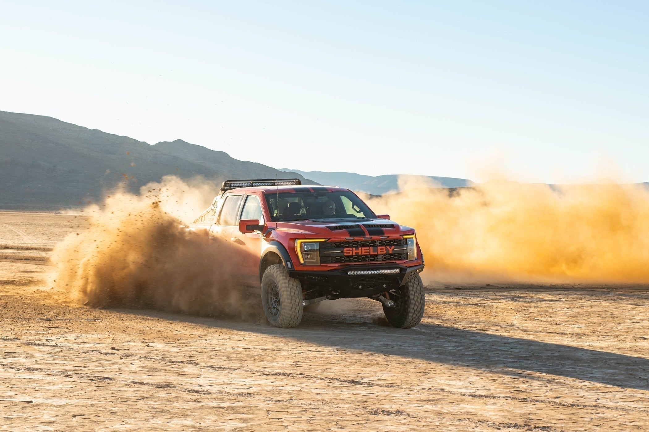 A red Shelby  F-150 truck kicks up dust in the middle of the desert