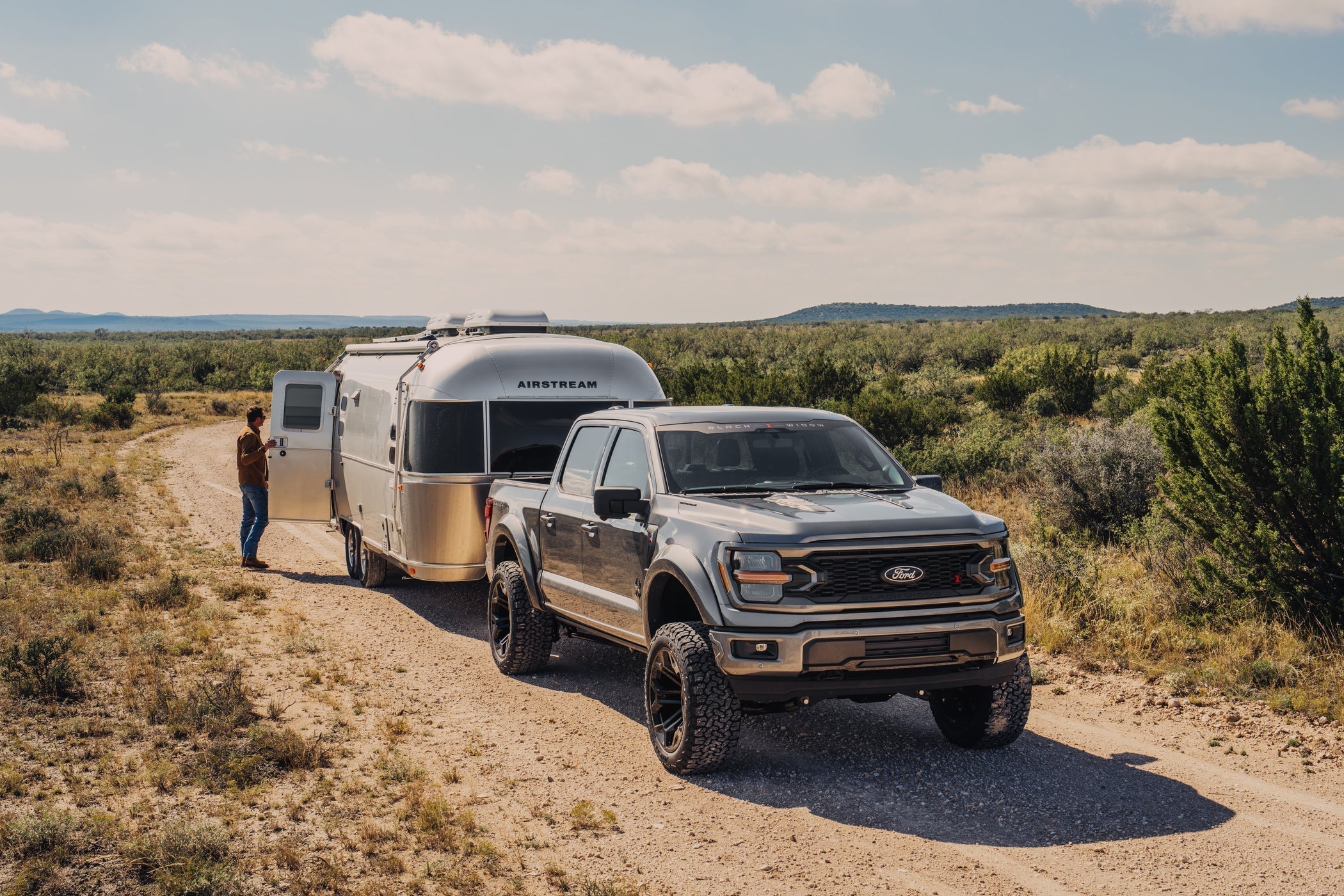A Black Widow F-150 truck towing an Airstream camper in a desert scene.
